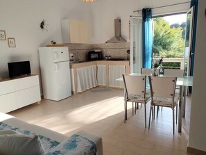 Eine kompakte Küche mit Kühlschrank, Mikrowelle und Herd, ein Essbereich mit Stühlen und Tisch sowie ein Sofa im Wohnbereich.