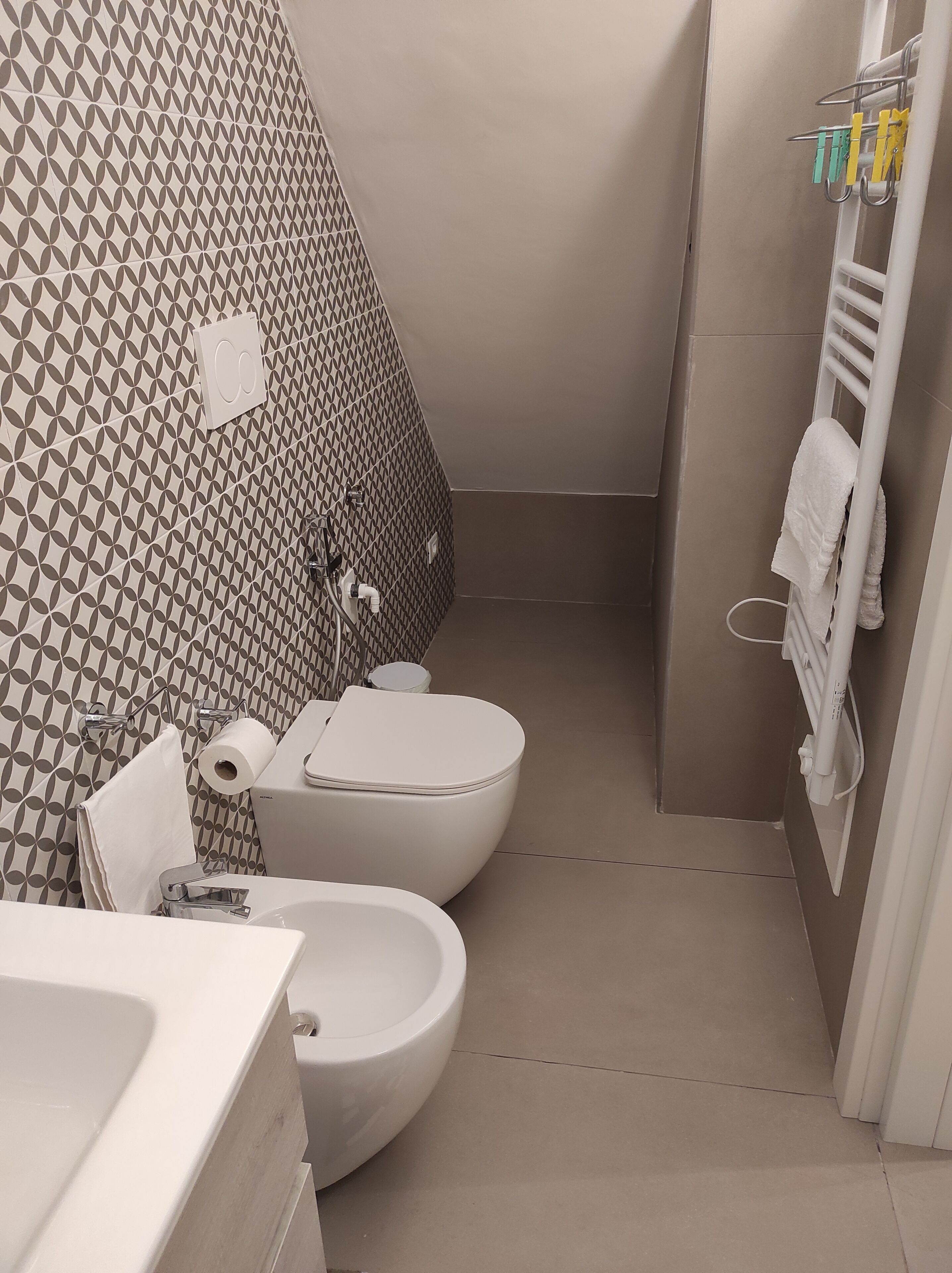 A bathroom with a patterned wall, a toilet, a bidet, and a towel rack.