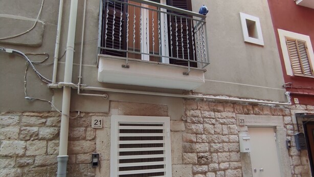 Un edificio con balcón, rejilla de ventilación y puerta con placa numérica.