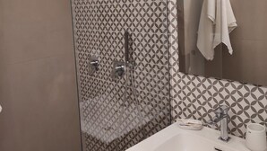 Un baño moderno con ducha de vidrio, un lavabo blanco y un espejo con una toalla colgada en la pared.