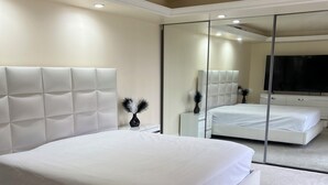 A modern bedroom with a large bed, a mirror, a flat-screen TV, and a white nightstand. - 2-bedroom townhome in peaceful Fort Myers with AC (Fort Myers)