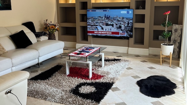 A living room with a television, a white sofa, a coffee table, and a decorative rug. - 2-bedroom townhome in peaceful Fort Myers with AC (Fort Myers)