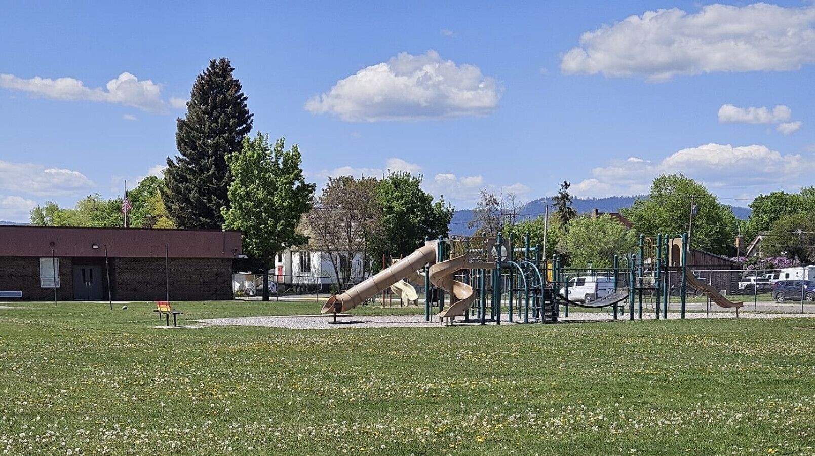 A playground with slides and climbing structures, surrounded by a grassy field and trees.