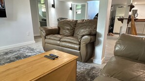 A living room with a leather sofa, a wooden coffee table, and a television mounted on the wall. - Short walk to downtown & Flathead Lake (Polson)