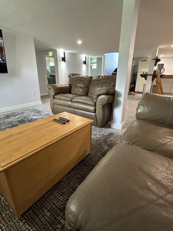 A living room with a leather sofa, a wooden coffee table, and a television mounted on the wall.