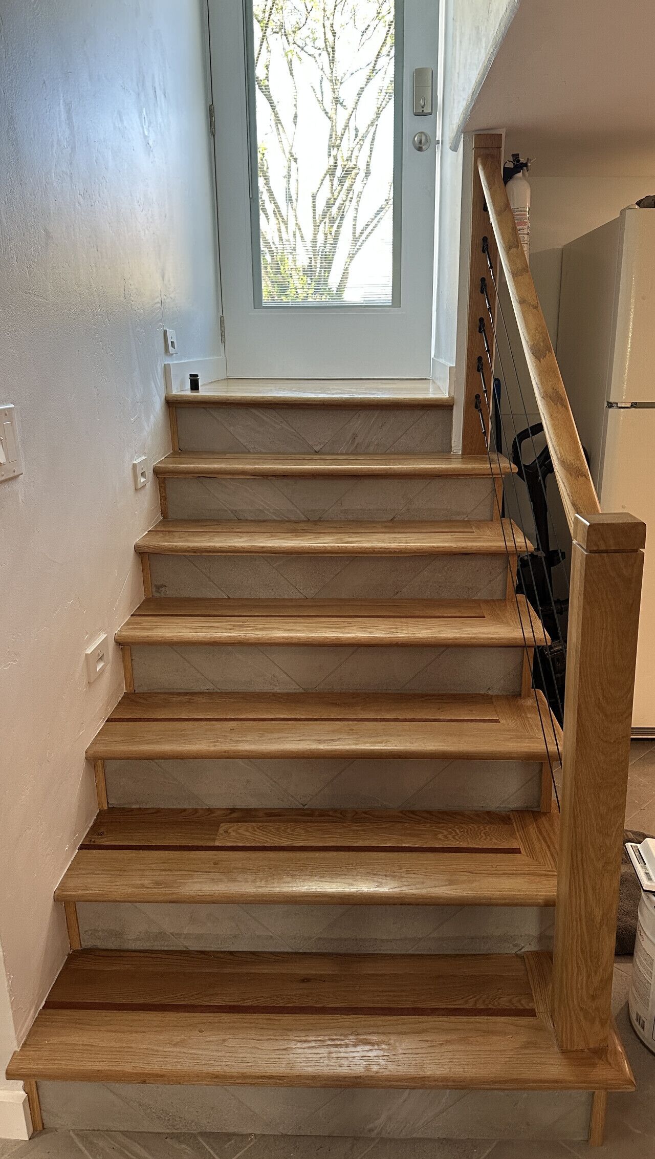 A wooden staircase with a handrail, leading to a door with a view of trees outside.