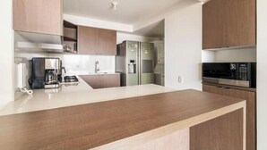 A modern kitchen with wooden cabinets, a stainless steel refrigerator, a coffee maker, and a microwave. - Luxo no Vale do Lili (Cali)