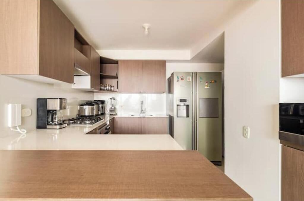 Une cuisine moderne dotée d’un îlot central, d’appareils électroménagers en acier inoxydable et de meubles de rangement en bois.