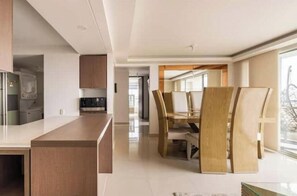 A modern kitchen with a central island, a dining area with a wooden table and chairs, and a view through a large window. - Luxo no Vale do Lili (Cali)