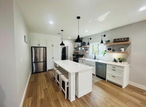 A modern kitchen with white cabinetry, stainless steel appliances, and a wooden floor. - Cozy Greers Ferry Getaway (Clinton)