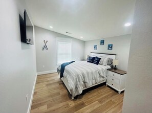 A bedroom with a bed, nightstand, wall-mounted TV, and a window with blinds. - Cozy Greers Ferry Getaway (Clinton)