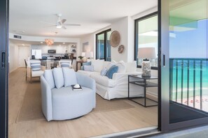 A modern living room with a sofa, a dining area, and a kitchen. There is a balcony with a view of the ocean. - 17th-Floor Gulf View Condo | Heated Pool, Hot Tub (Panama City Beach)
