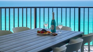 A wooden table with a bottle of champagne, two glasses, and a fruit platter on a balcony overlooking the ocean. - Gulf View Oasis and Beach Chairs (Panama)