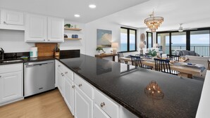 A modern kitchen with white cabinets, a black granite countertop, and a dining area with a view of the ocean. - Gulf View Oasis and Beach Chairs (Panama)