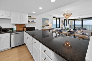 A modern kitchen with white cabinets, a black granite countertop, and a dining area with a view of the ocean. - Panoramic View, Free Beach Chairs (Panama)
