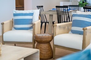 Two wicker chairs with white cushions and blue-striped pillows, a wooden side table, and a dining area with chairs and a table in the background. - Panoramic View & Beach Chairs (Panama)