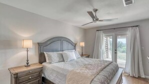 Un dormitorio con cama, dos mesitas de noche con lámparas, un ventilador de techo y una ventana con cortinas.