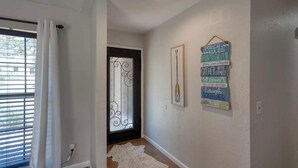 Un pasillo con una puerta blanca, una ventana con persianas y un letrero decorativo en la pared.