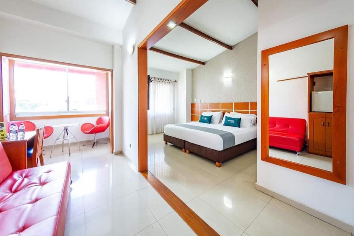 Habitación de hotel con una cama, un sofá rojo, una zona de comedor con sillas y una ventana.