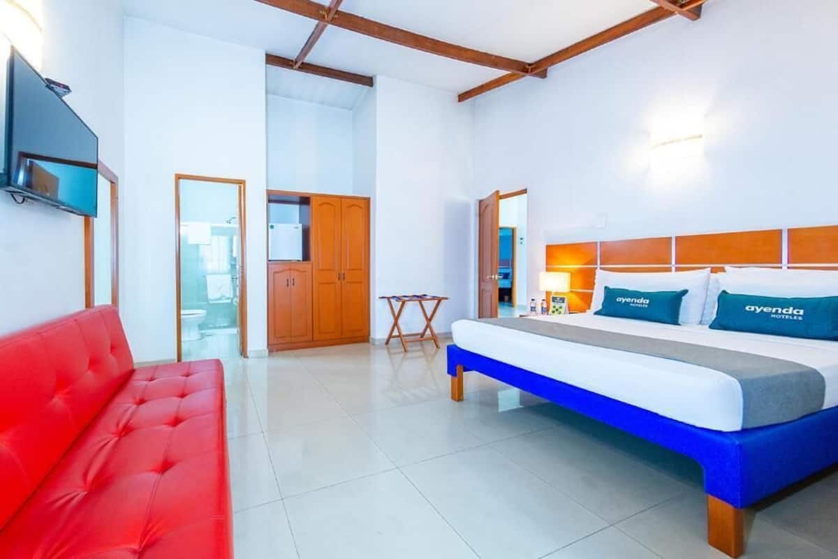 Una habitación de hotel con una cama, un sofá rojo, un televisor y un armario de madera.