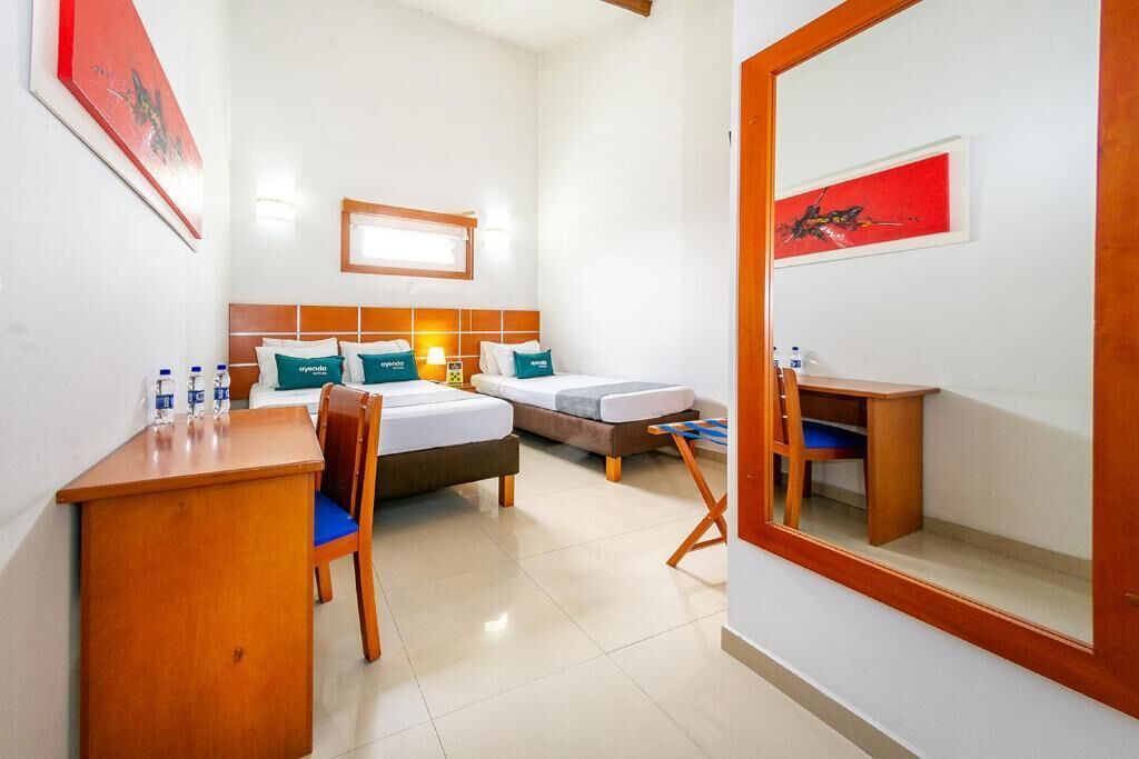 A hotel room with two beds, a desk, a chair, a mirror, and artwork on the walls.