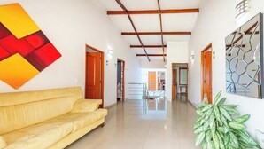 A spacious hallway with a yellow sofa, a large abstract painting, and a potted plant.