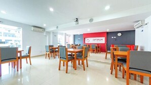 A modern hotel lobby with wooden tables and chairs, a red wall with the hotel name, and a large window.