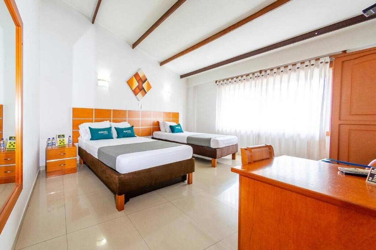 Habitación de hotel con dos camas, un escritorio, un espejo y una ventana con cortinas.