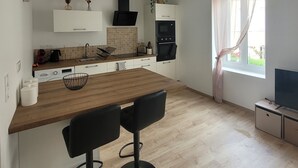 A modern kitchen with a wooden island, two bar stools, a built-in oven, and a TV on a stand.