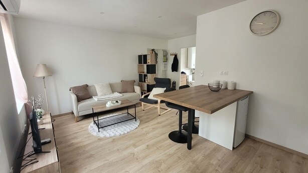 A modern living room with a sofa, coffee table, dining table, and a kitchen area in the background.