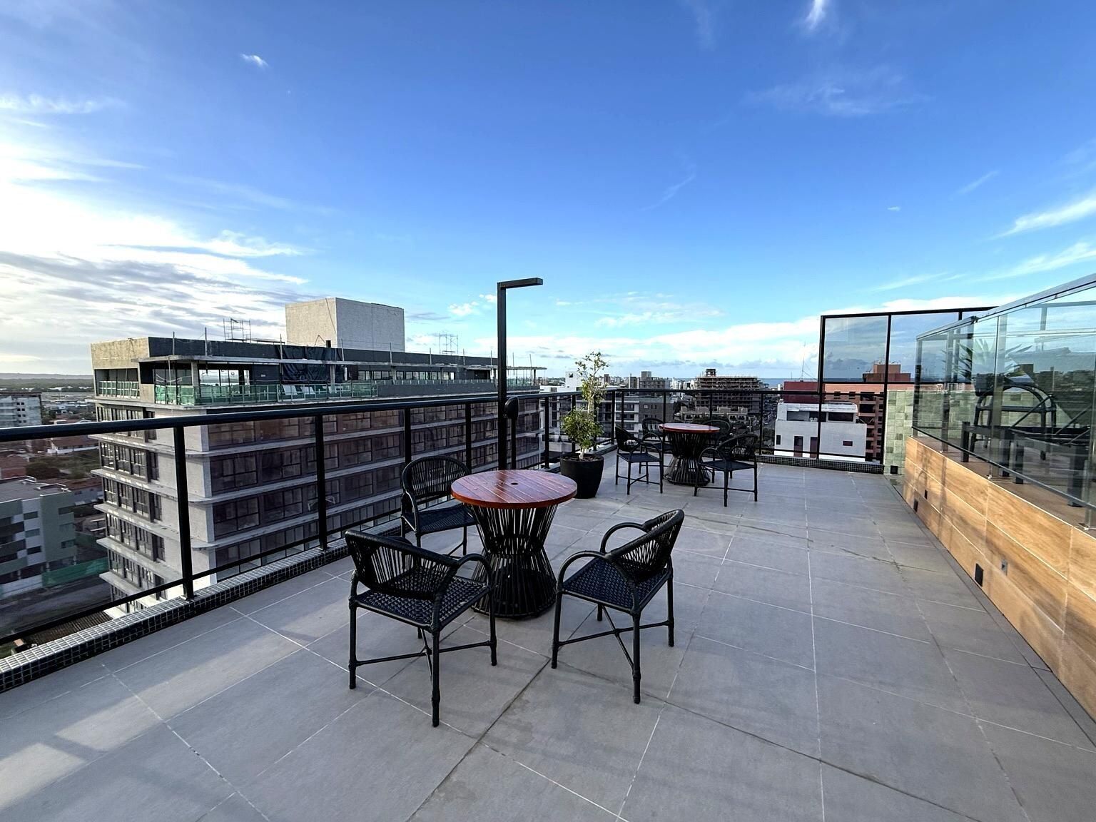 A rooftop terrace with a round table and chairs, a potted plant, and a glass railing overlooking a cityscape.