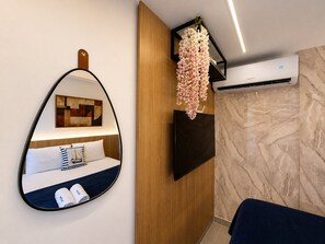 A modern hotel room with a bed, a hanging flower arrangement, a mounted TV, and an air conditioning unit. - Emunah Flat Luxo Cabedelo  Rooftop (Cabedelo)