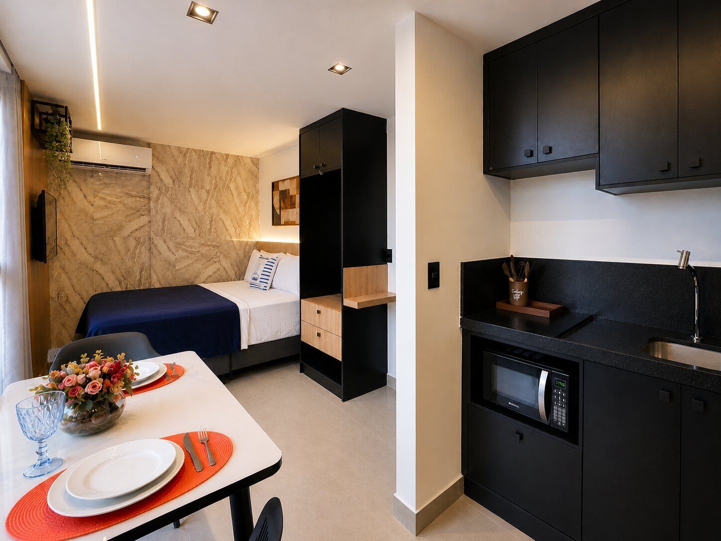 Una habitación compacta con cama, kitchenette pequeña y comedor con mesa lista para dos.