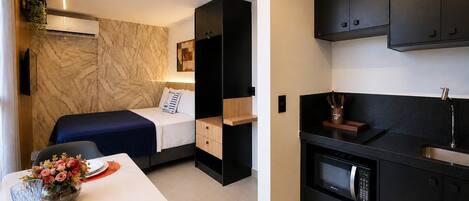 Una habitación compacta con cama, kitchenette pequeña y comedor con mesa lista para dos.