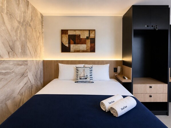 Habitación de hotel con cama, mesita de noche, teléfono en la pared, un cuadro y un armario.