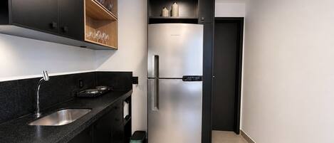 A modern kitchen with a stainless steel refrigerator, black countertops, and wooden shelves.