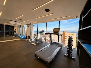 Un gimnasio moderno con equipo de ejercicio, ventanas amplias y vistas a la ciudad.