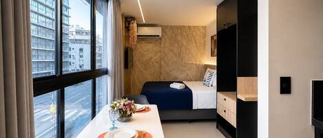 A modern hotel room with a bed, bedside table, and a view of the city.