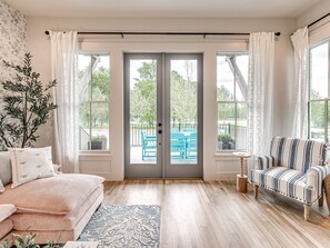 Ein Wohnzimmer mit einer Couch, einem gestreiften Sessel, einem Couchtisch und Blick durch eine Glastür auf einen Außenbereich mit Sitzgelegenheiten.