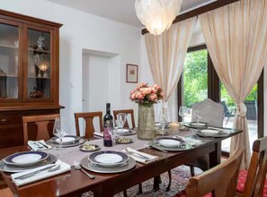 A dining room with a wooden table set for four, a cabinet with glass doors, and a vase with flowers. - Villas Casa Bianca & Maria Residence - Four Bedroom Villa with Outdoor Pool (Krnica)