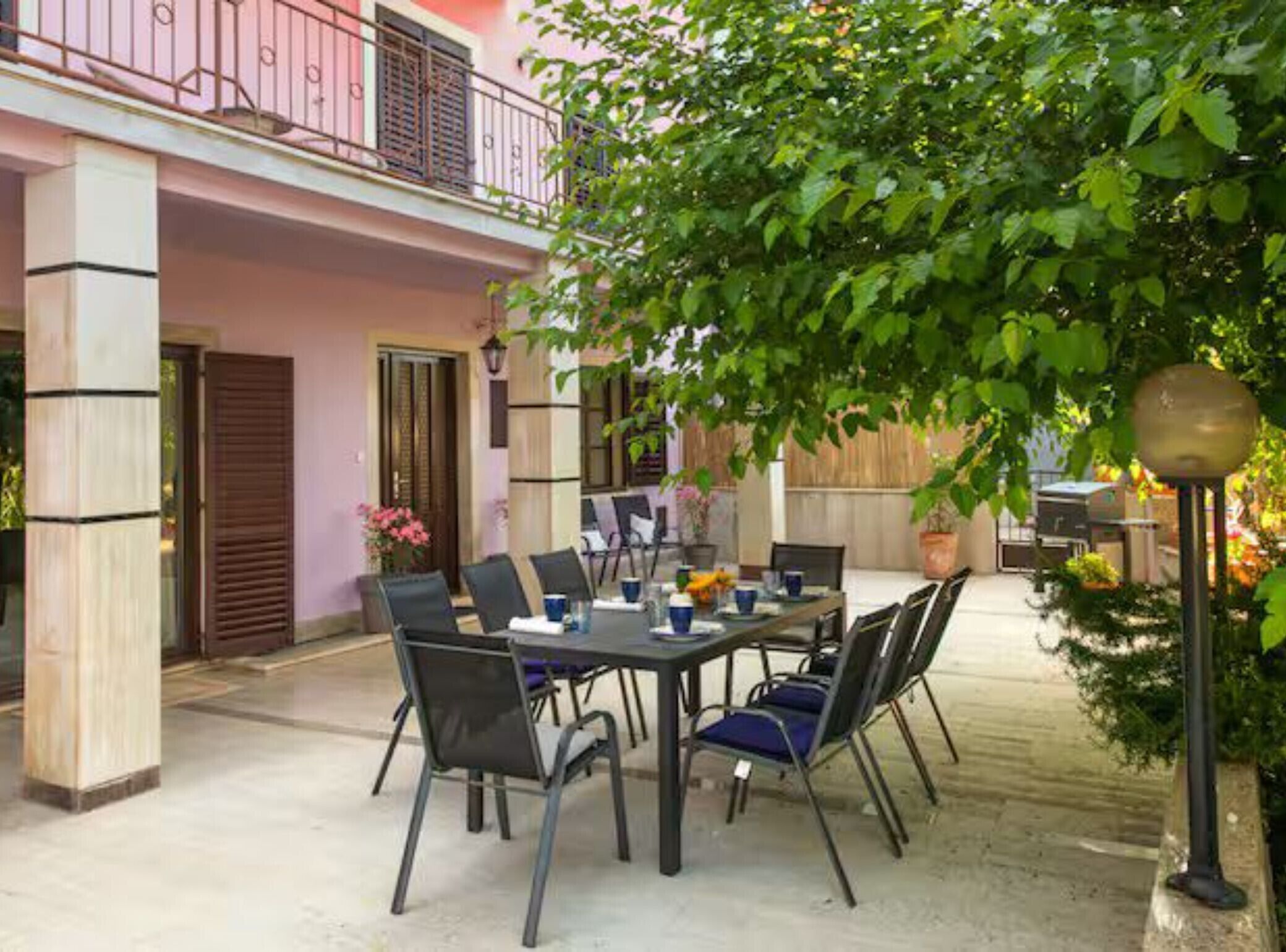 An outdoor patio with a table and chairs, a balcony, and a tree providing shade.