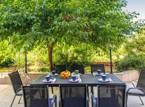 Ein Essbereich im Freien mit einem Tisch für vier Personen, umgeben von Stühlen, unter einem Baum.