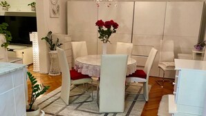 A modern dining area with a round table, white chairs, and a vase of red flowers. - Comfort Studio Apartment - Studio Apartment with Garden View (Kastel Luksic)