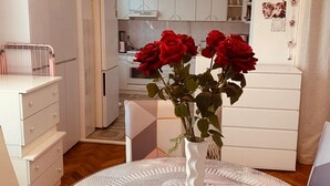 A room with a dining table, a white vase with red roses, and a kitchen in the background. - Comfort Studio Apartment - Studio Apartment with Garden View (Kastel Luksic)