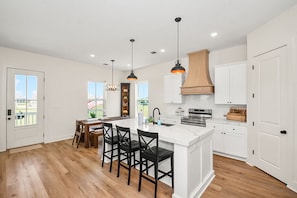 Une cuisine moderne dotée d’un îlot central, de luminaires suspendus et offrant une vue sur l’extérieur.