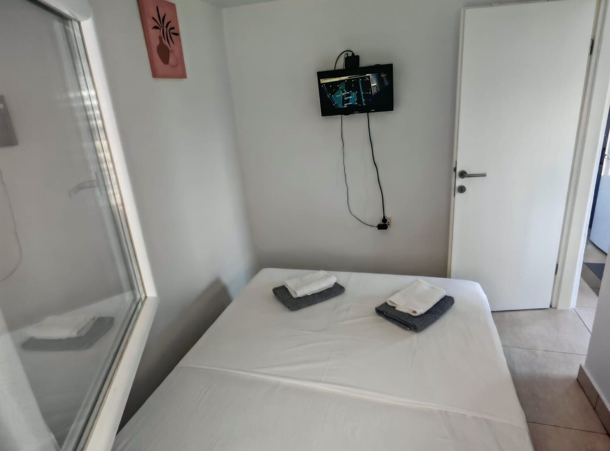 A hotel room with a bed, a wall-mounted TV, a door, and a window.