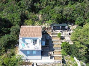 A white building with a tiled roof, surrounded by dense green forest. - Green House - Two-Bedroom Apartment with Terrace and Sea View (Sobra)