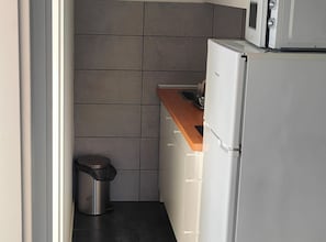 A compact kitchen with a stainless steel trash bin, a microwave, and a refrigerator. - Green House - Two-Bedroom Apartment with Terrace and Sea View (Sobra)
