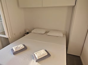 A hotel room with a bed, two pillows, a nightstand with a lamp, and two towels on the bed. - Green House - Two-Bedroom Apartment with Terrace and Sea View (Sobra)