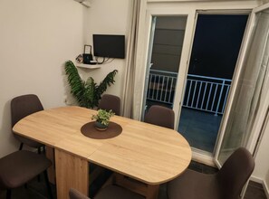 A dining area with a wooden table, six chairs, a potted plant, and a TV on the wall. - Green House - Two-Bedroom Apartment with Terrace and Sea View (Sobra)
